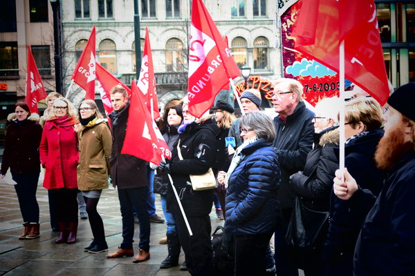 En gruppe demonstranter deltar i kampanjen Tannhelse for alle. De holder oppe røde flagg. Foto.