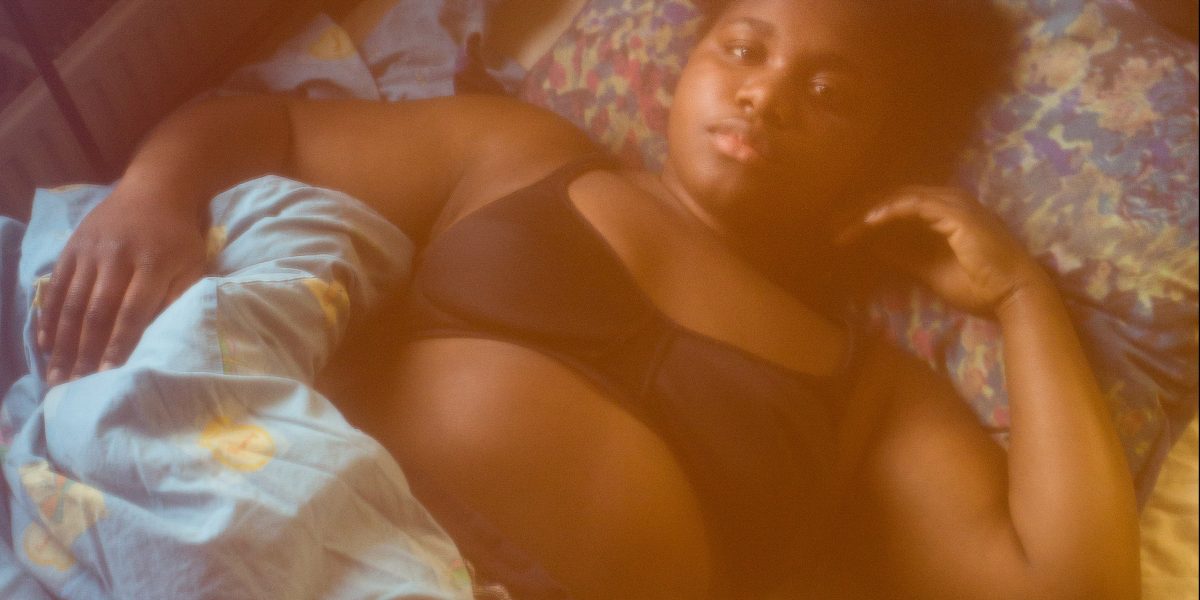 Kvinne ligger på en seng, med en dyne delvis over seg. Foto.